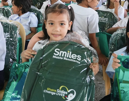 A child poses with school bag, with log of 'Smiles Mobile Remittance' visible