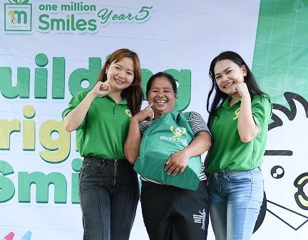 Three people in green shirts pose in front of Smiles Year 5 'one million smiles' logo.